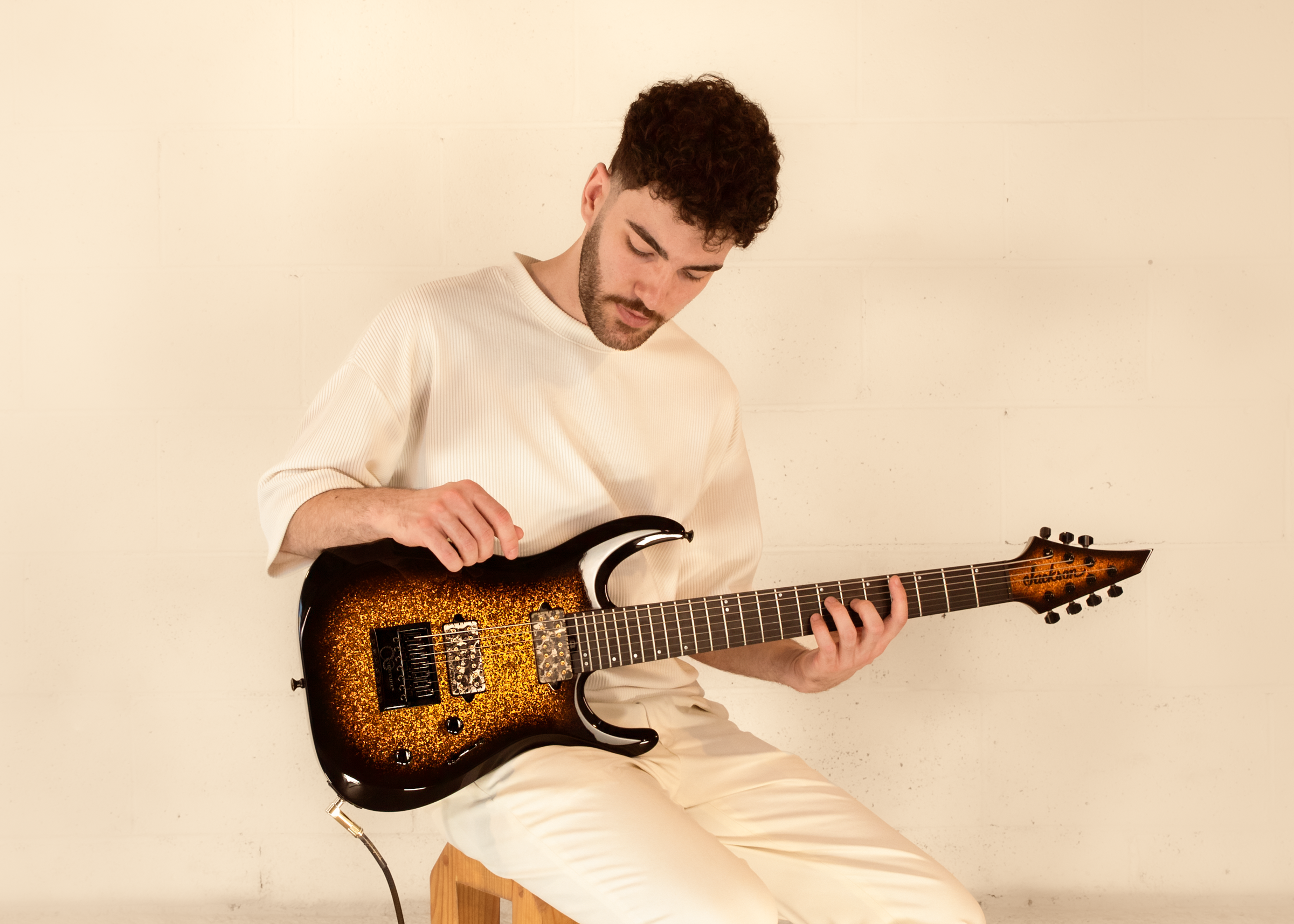 KEYAN playing an electric guitar on a stool against a plain background